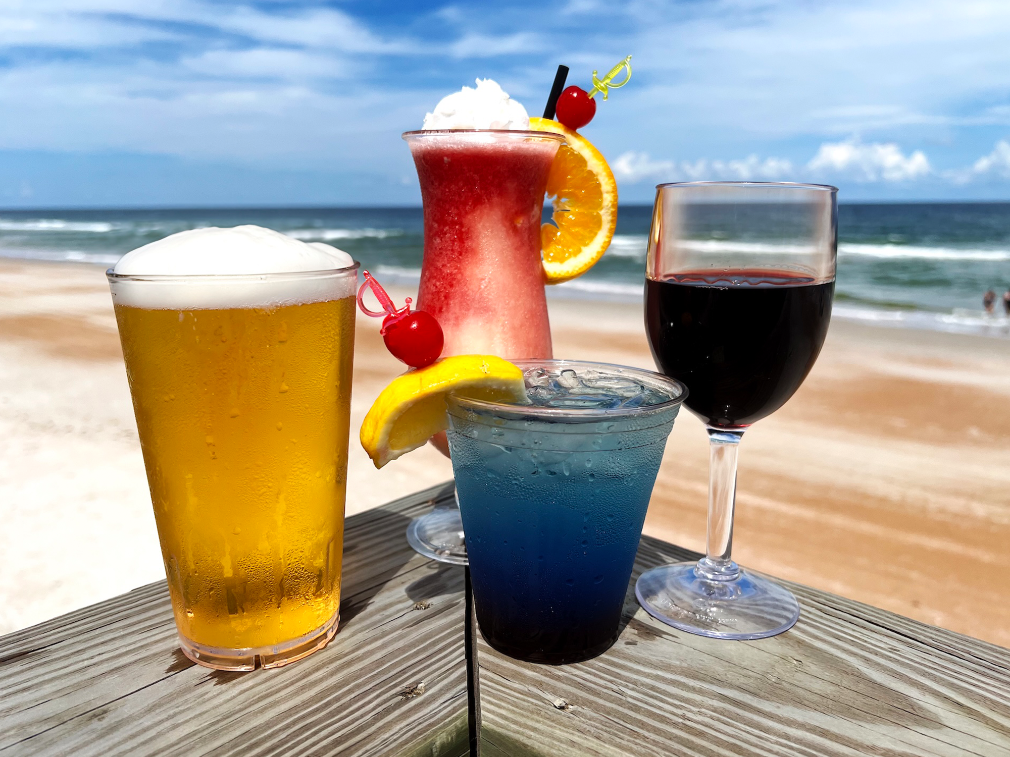 Four glasses of different drinks on a beach setting with ocean view