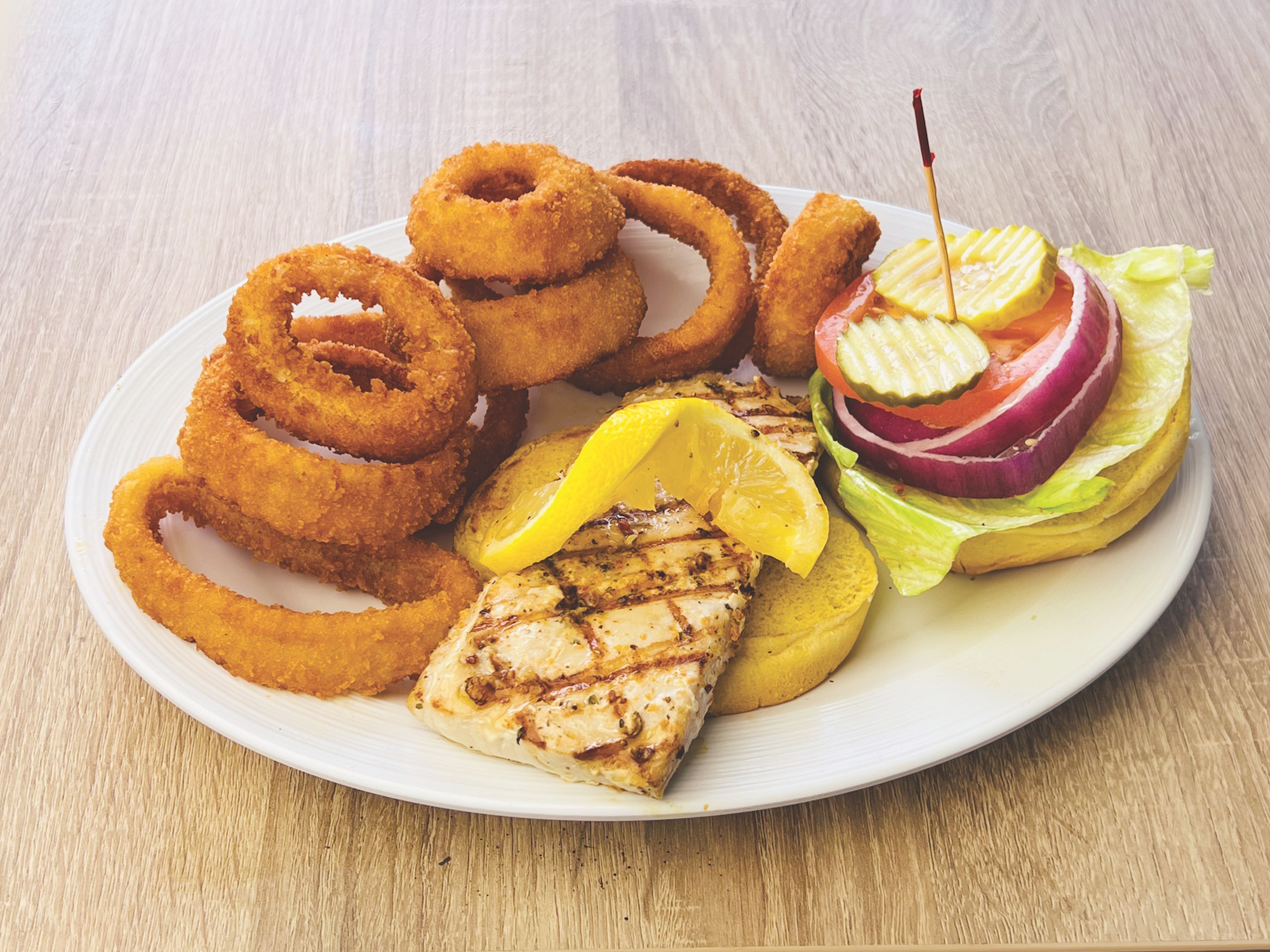 Platter of onion rings, grilled fish, lemon wedges, and pickled vegetables on a wooden surface.