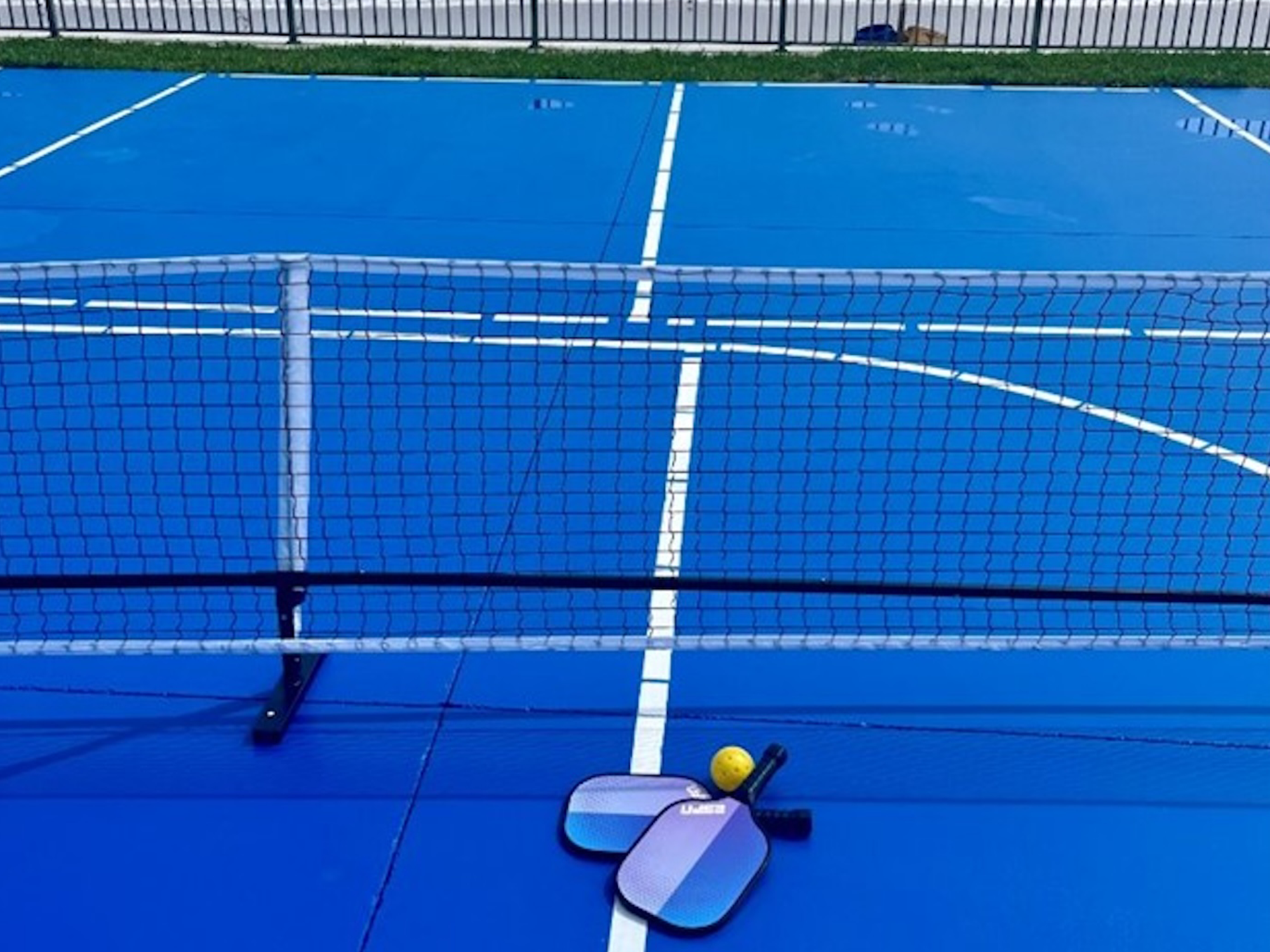 Blue pickleball court with paddle and ball on a sunny day