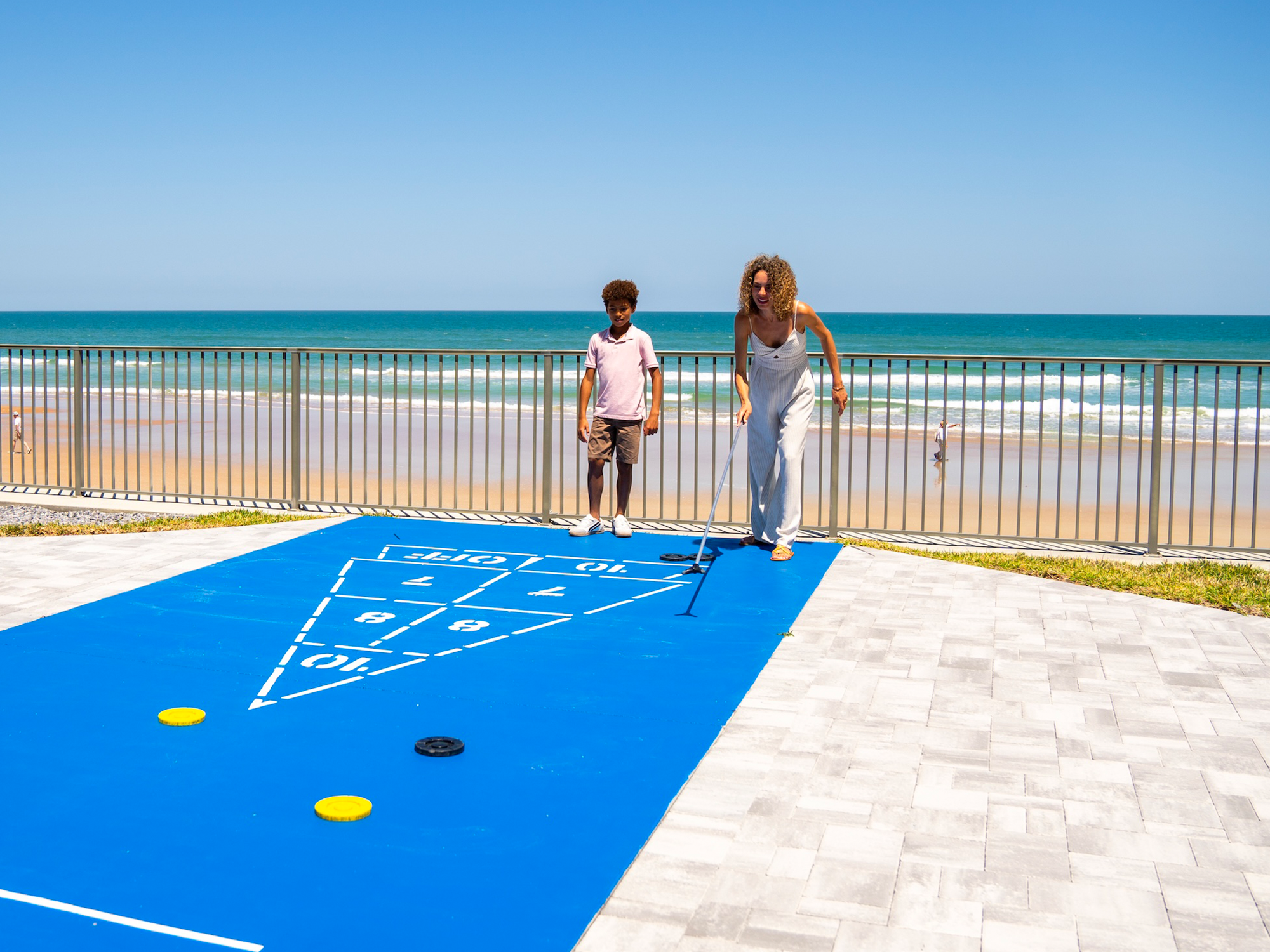 Mother and son playing shuffleboard on a deck with ocean view