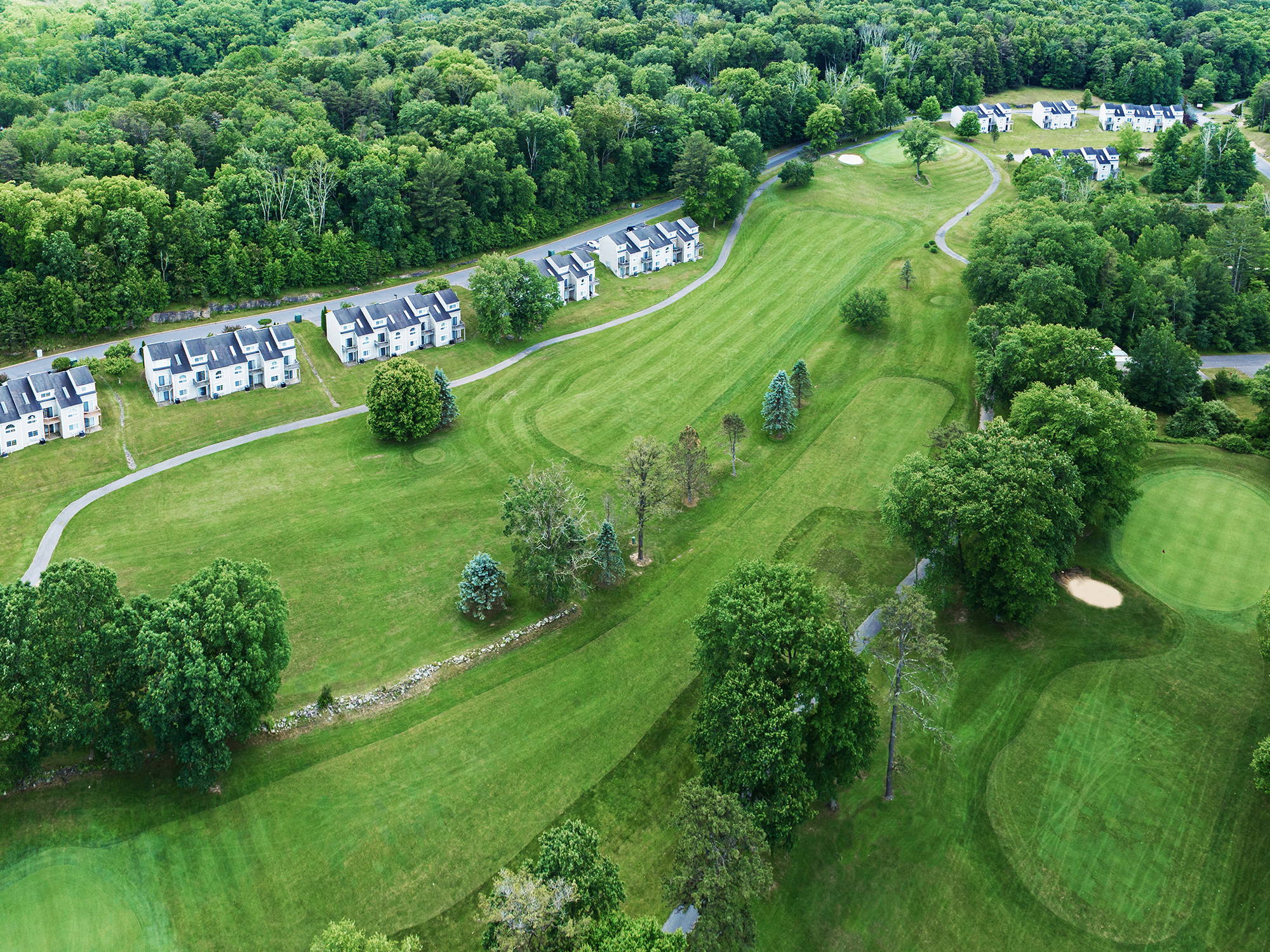 Aerial view of a golf course with clubhouse and residential buildings surrounded by trees.