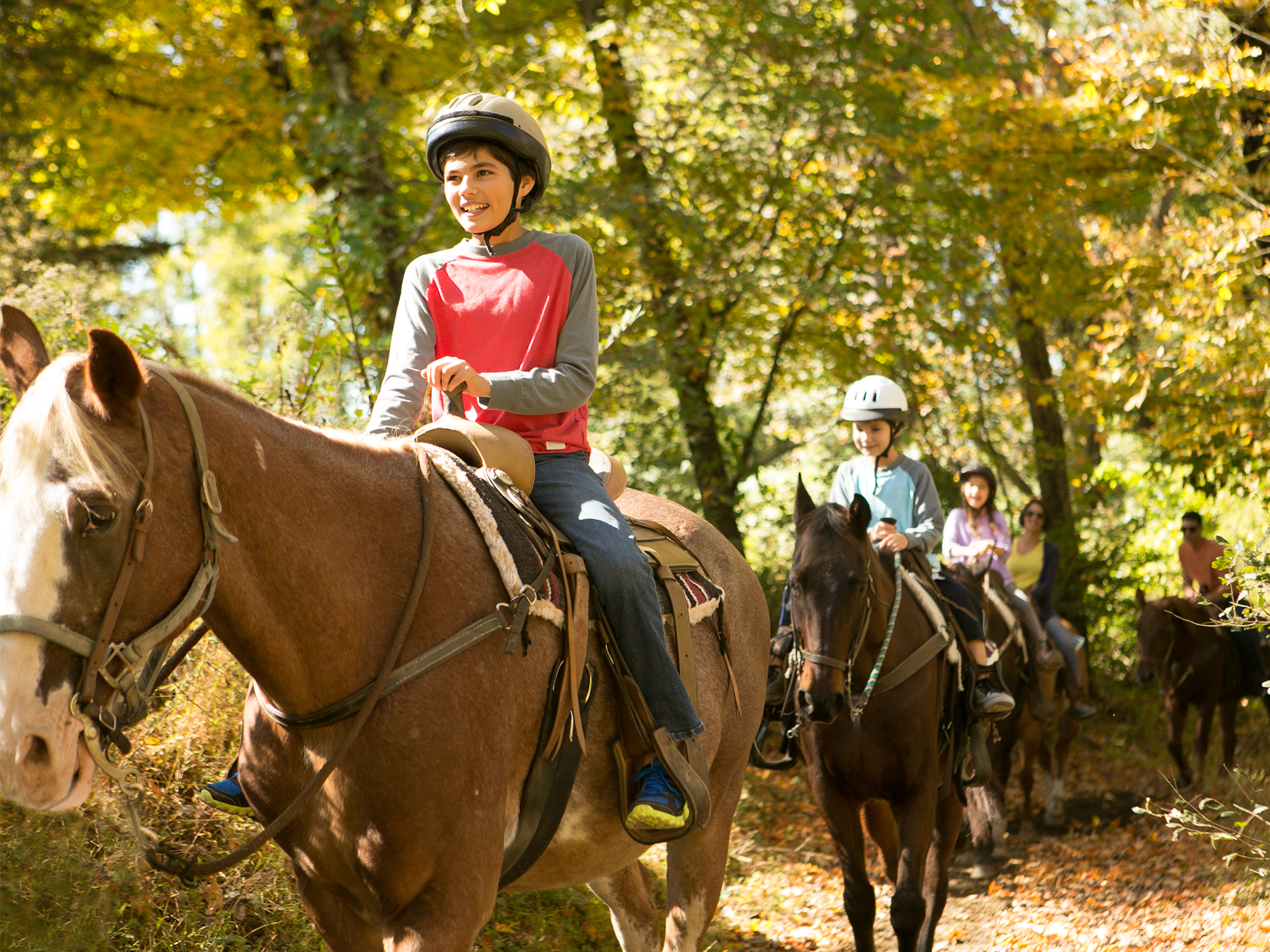 Parents and kids riding horses in a forest during autumn.