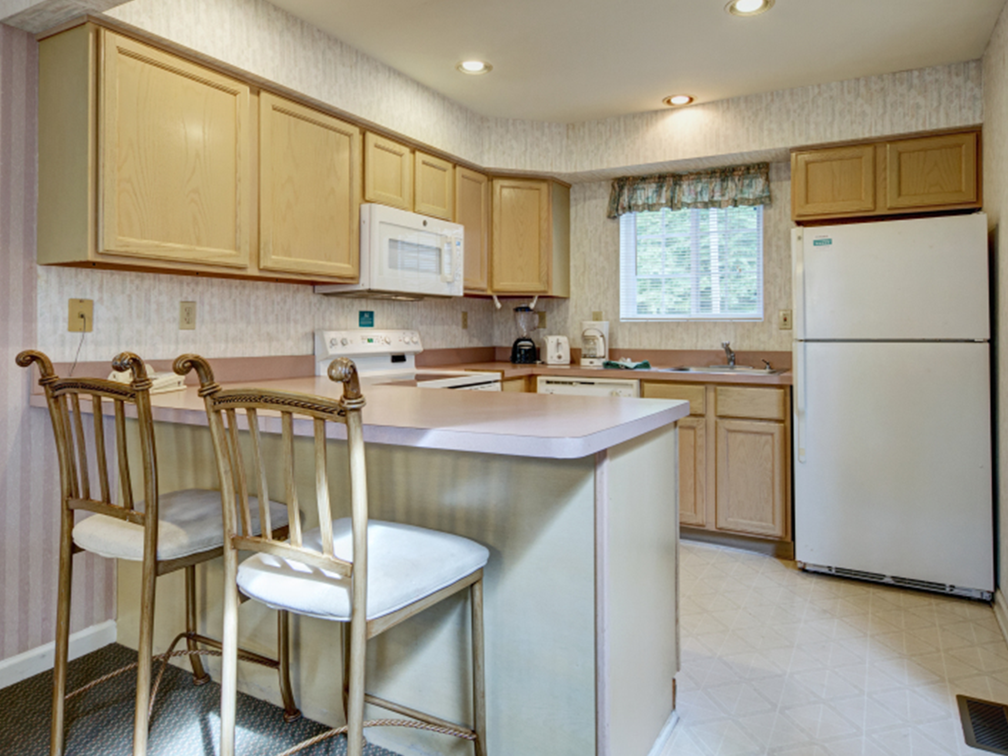 Kitchen with wooden cabinets, white appliances, and a breakfast bar.