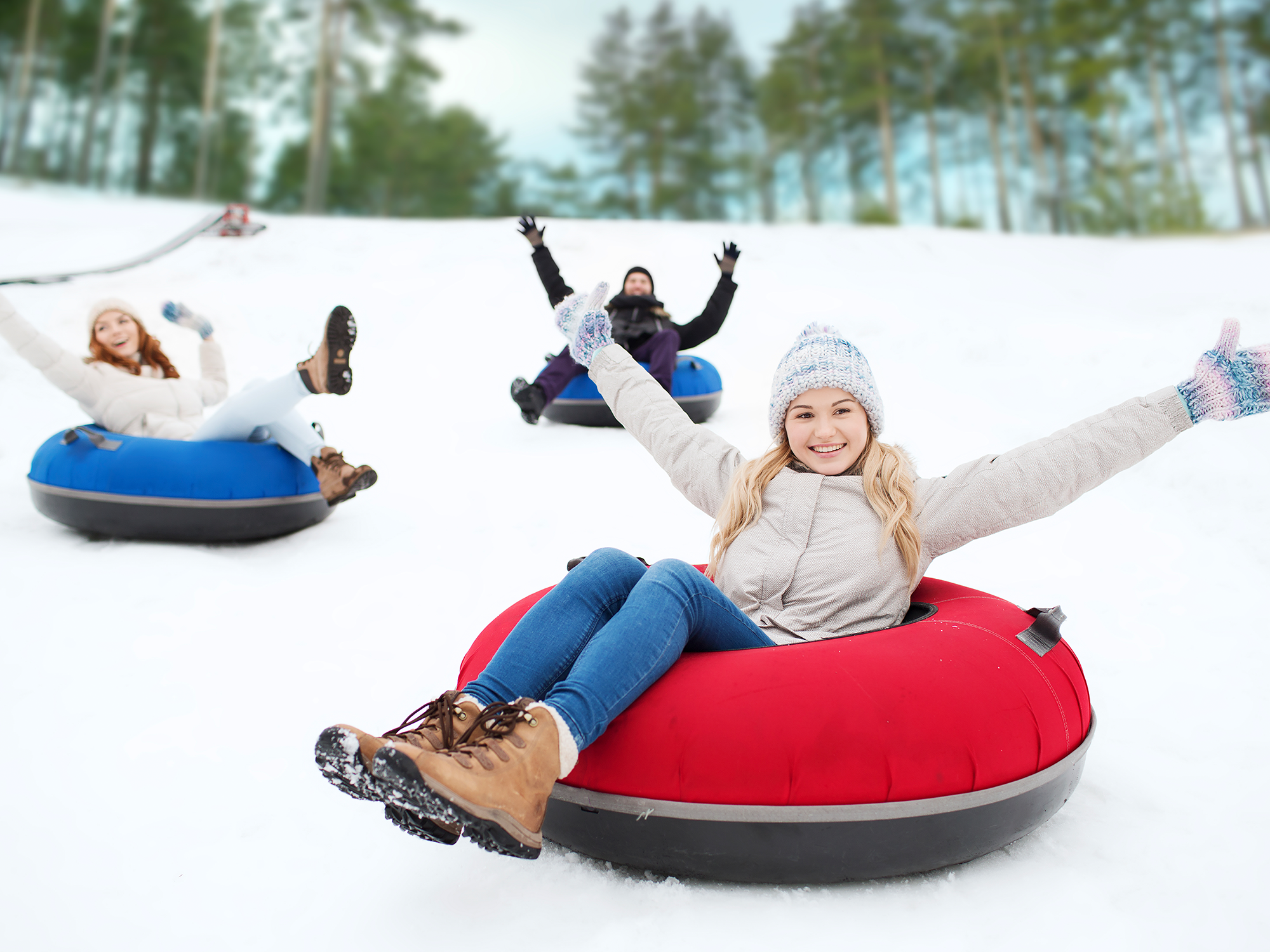 People enjoying snow tubing in a snowy landscape with trees in the background.