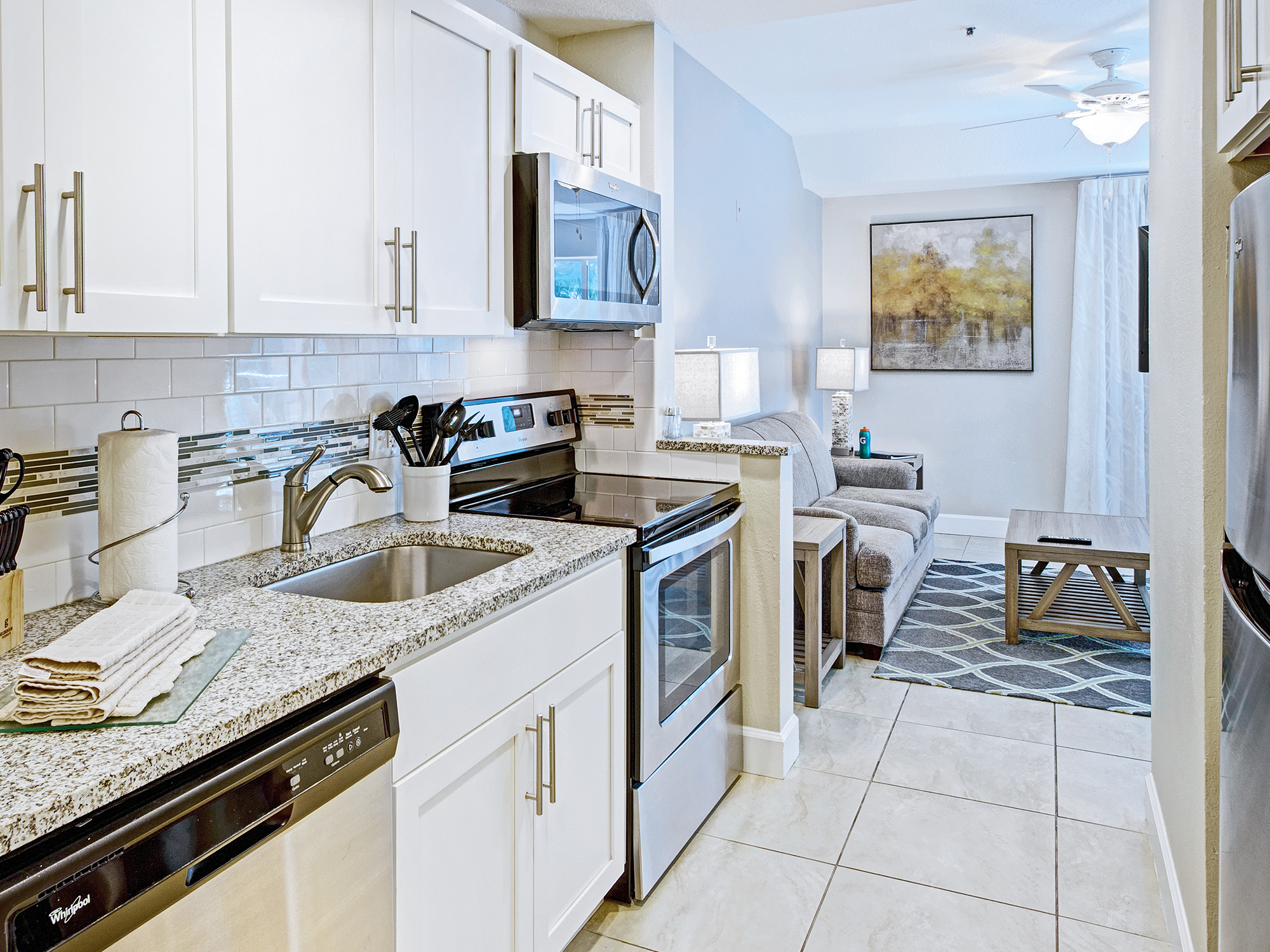 Modern kitchen and living room area with white cabinets and stainless steel appliances.