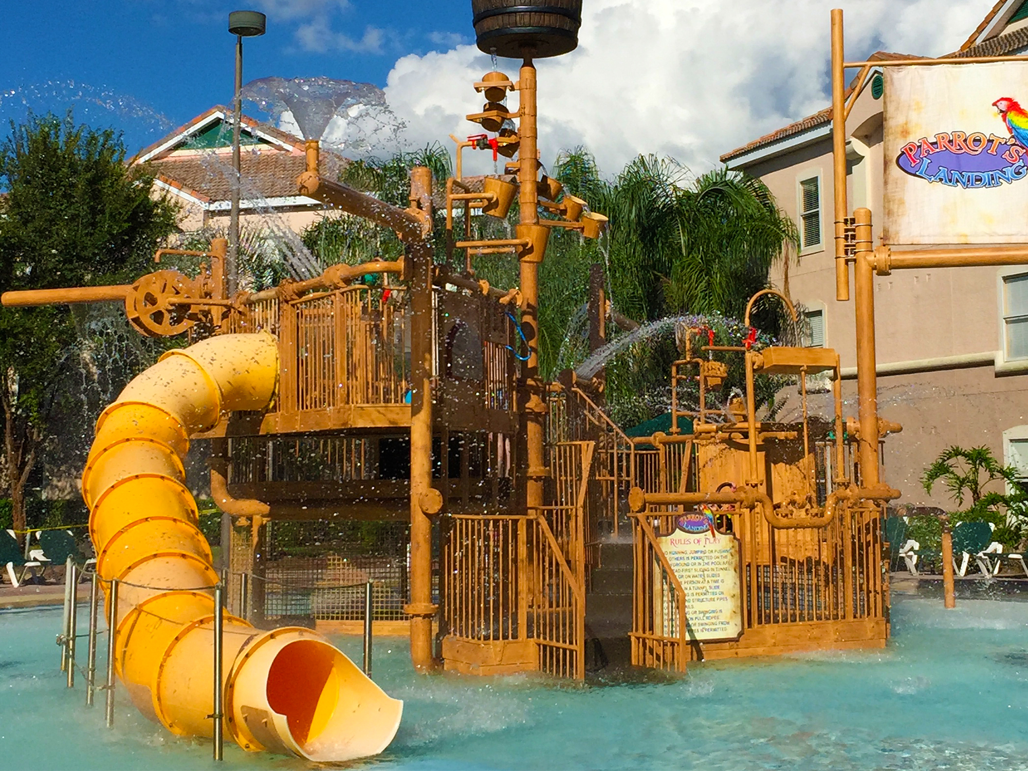 Water playground with yellow slide and wooden structure in a pool area.